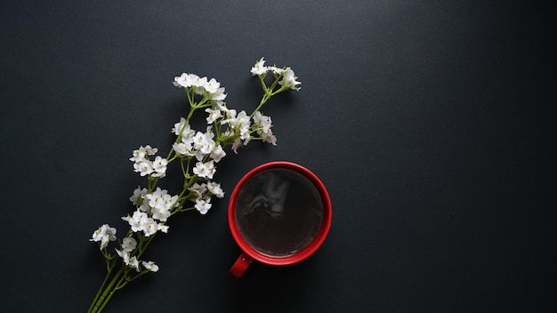 A red coffee cup and white flowers on black leather