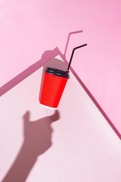 ピンクの背景の黒いストローと影の赤いコーヒーカップ