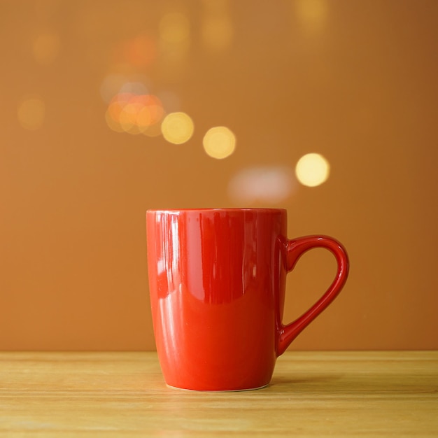 Red coffee cup on wooden desk on brown background with bokeh