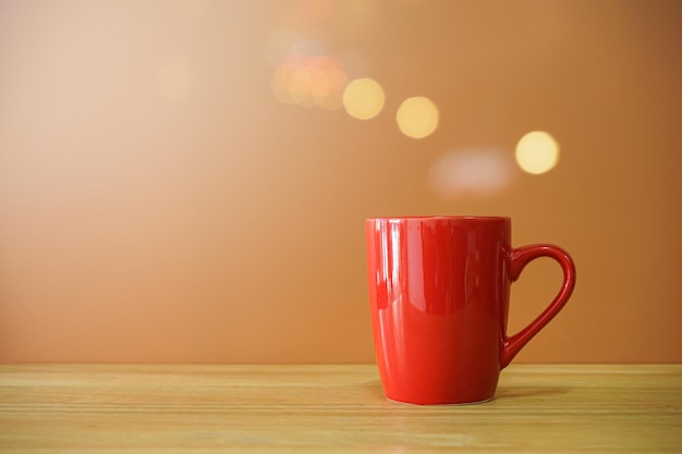 Red coffee cup on wooden desk on brown background with bokeh