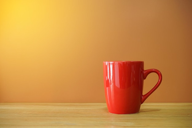 Red coffee cup on wooden desk with brown background