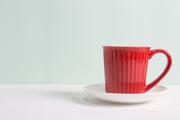 Red coffee cup on wooden table over pastel green background