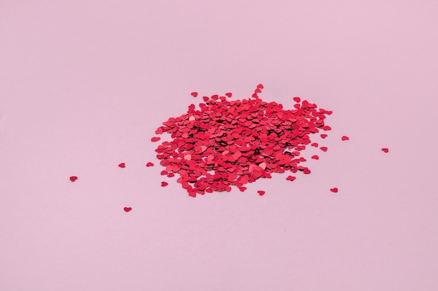 Red confetti pile on pink background. Confetti in shape of hearts.