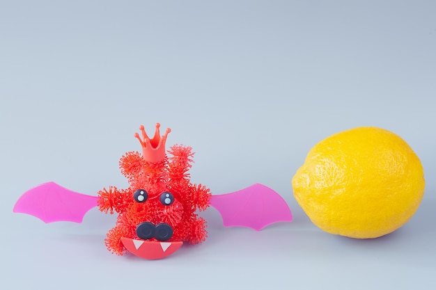 Red coronavirus in the form of a bat from a children's designer with Velcro on a gray background. lemon near the bat. wild animals concept - source of infection.