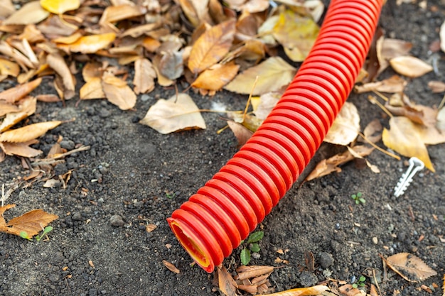 Red corrugated hose for electrical wiring on the ground. Close-up, selective focus