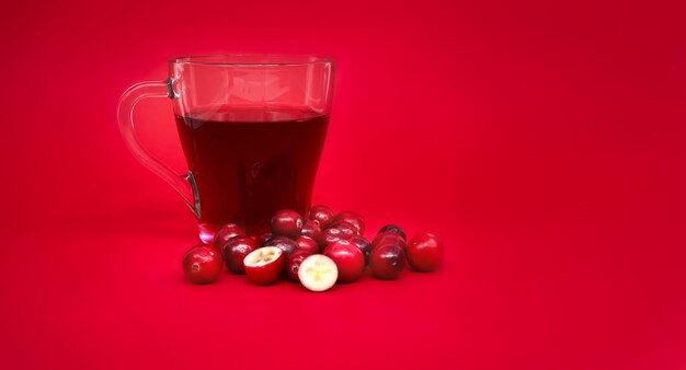 Red cranberries and transparent cup containing red cranberry juice against a vibrant red background