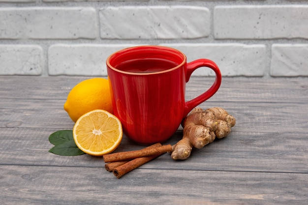 Tazza rossa di tè nero o verde caldo con limone e zenzero su un fondo di legno. ingredienti contro influenza e virus. medicina naturale.