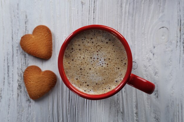 Tazza rossa di cacao caldo e biscotti a forma di cuore su una superficie di legno