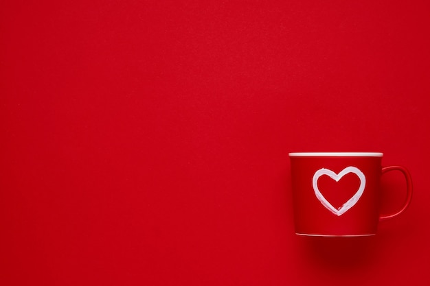Red cup mug with with painted heart on scarlet or red table. Flat lay composition. Valentines Day concept. Top view, copy space.