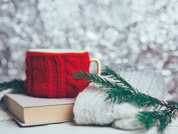 Tazza rossa di tè o caffè con i rami dell'albero di natale e del libro