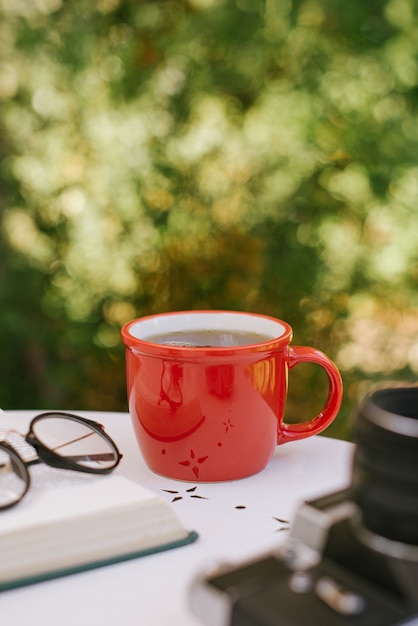 Red cup of tea on the table next to a book and glasses in anticipation of autumn