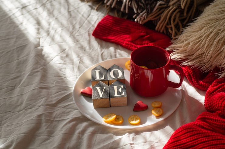 Photo red cup of tea with kumquat on the plate and two hearts cookies with the word love on a white bed