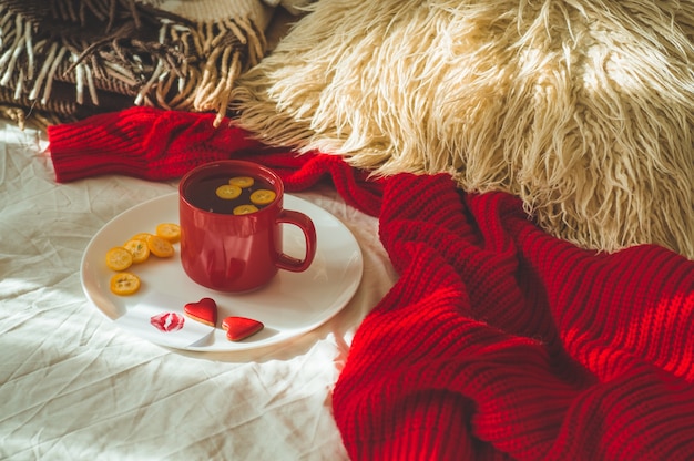 Red cup of tea with kumquat and two hearts cookies on a white bed