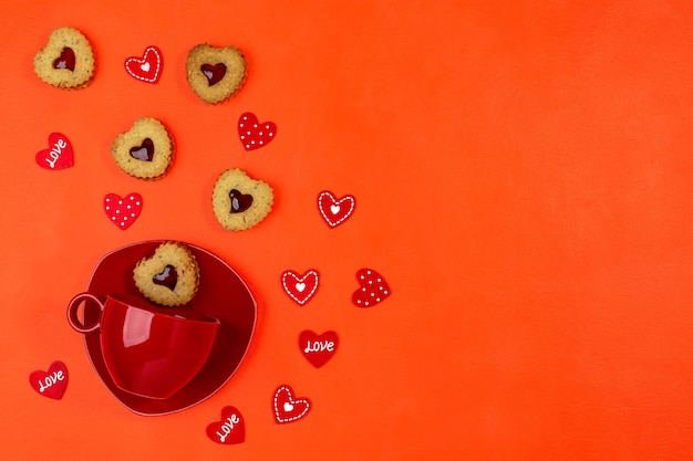 Tazza rossa con biscotti a forma di cuore di biscotti piattino e linzer su sfondo rosso. biglietto di auguri di san valentino