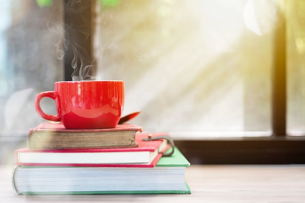 Red cup with smoke on top of stacked old books on wood table with window light. Merry Chri