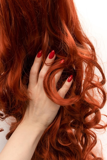 Рыжие вьющиеся волосы в руках женщины с красными ногтями