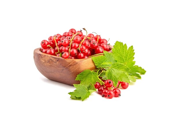 Red currant berries in wooden bowl with fresh green leaves isolated