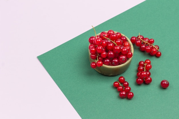 Red currant in a ceramic box. Geometric pink green background. Flat lay. Copy space