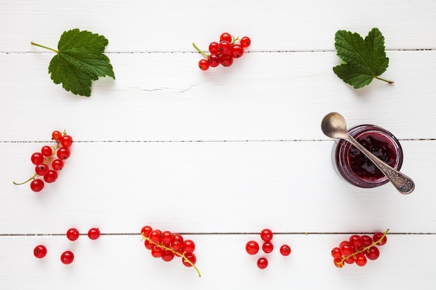 Фото Варенье из красной смородины и свежие ягоды красной смородины в качестве границы с копией пространства на белом столе