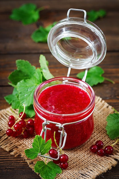 Red currant jam in a jar on a wooden surface. Tasty food.