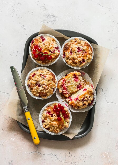 Red currant muffins with crumble in a baking tray on a light background top view