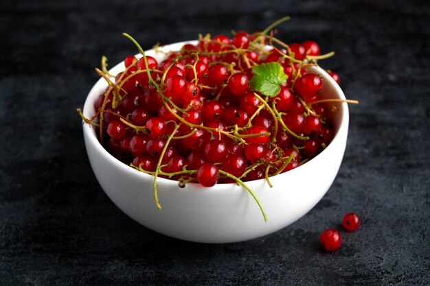 Red currant in a white bowl on the black table.