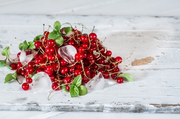 Red currant with ice and green leaves on white wood. Still life of food. 