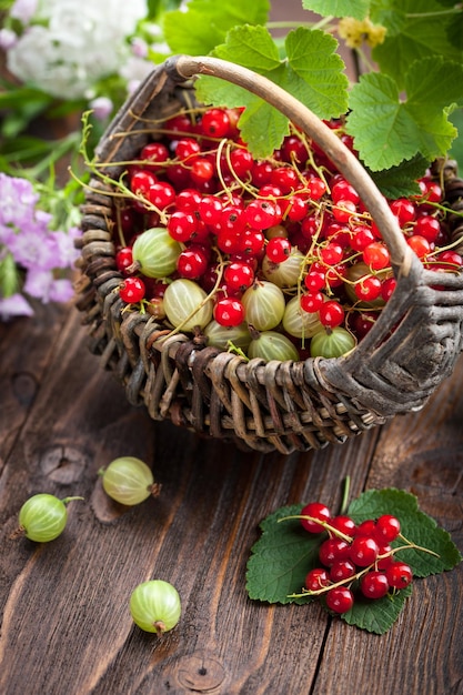 Photo red currantand and  gooseberry in the basket on wooden table