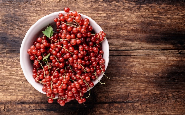 Red currants in a deep plate on a wooden background. Place for your text.