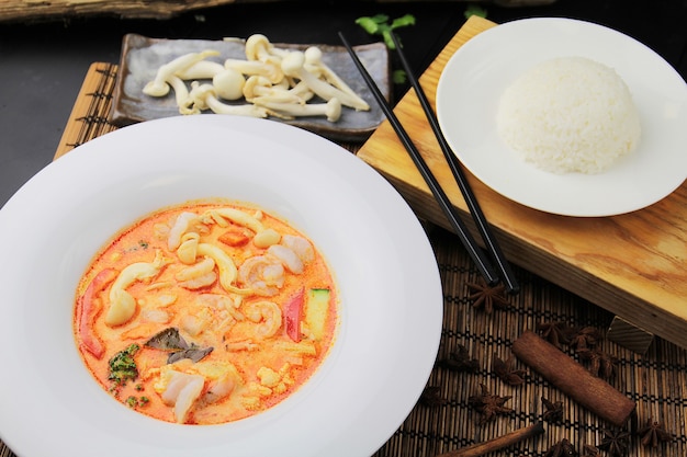 Red curry with shrimp on a white plate, rice and chopsticks