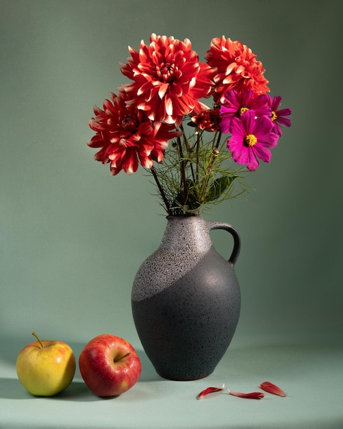 Red dahlias in a ceramic jug on the table Two apples