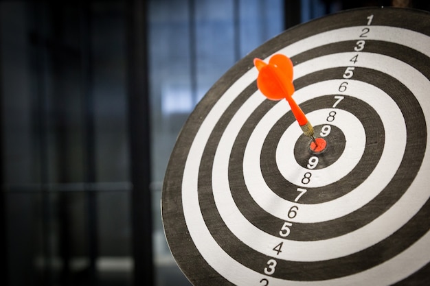 Red dart arrow hitting in the target center of dartboard on bullseye with sun light vintage style