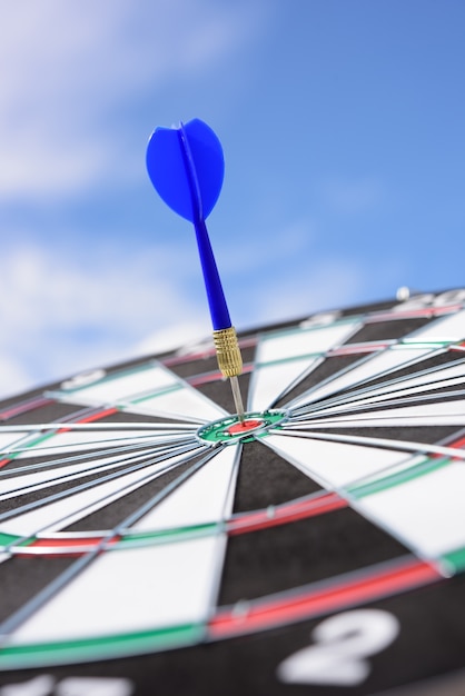 Red dart arrow hitting in the target center of dartboard with blue sky background