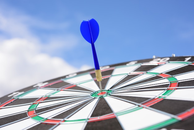 Red dart arrow hitting in the target center of dartboard with blue sky background