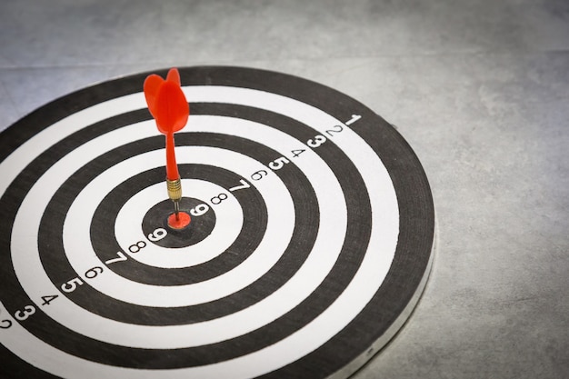 Red dart arrow hitting in the target center of dartboard.