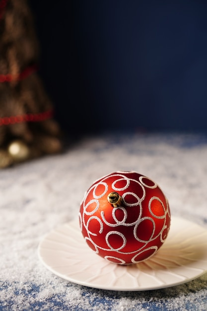 Decorazione rossa per l'albero di natale su un piatto bianco su sfondo blu con un albero di natale