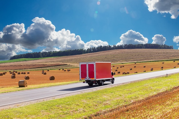 Red delivery track, van on the highway, against the background of a yellow harvested wheat field. There is a place for advertising