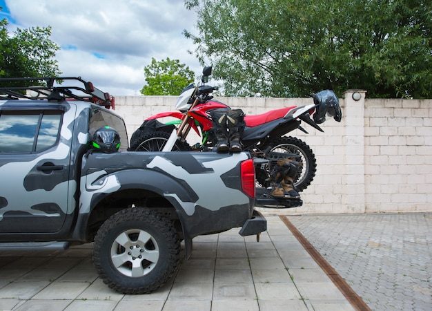 Red dirt bike motorcycle on the back of the camo truck with safety gear.