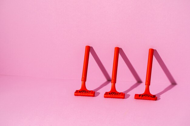 Red disposable razor on pink background, with copy space