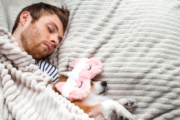 Red dog sleeps in a pink sleeping mask with his owner in the bed. Concept weekend and rest