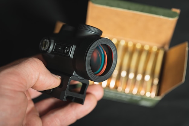 Red dot sight in hand and firearms 556x45mm ammo box closeup photo