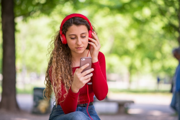 Red dressed teenager listening music from phone in a park