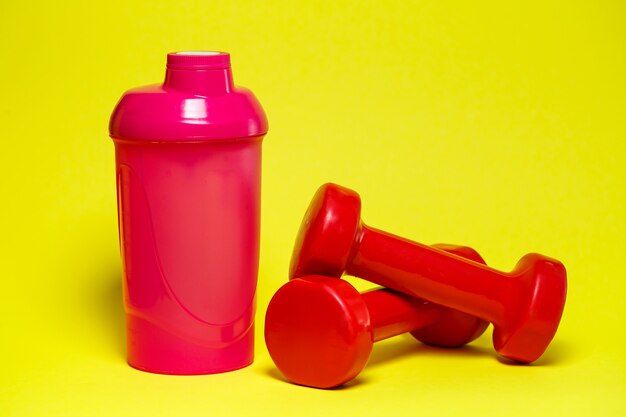 Photo red dumbbells, pink shaker, colored background, sports, energy drink, gym equipment