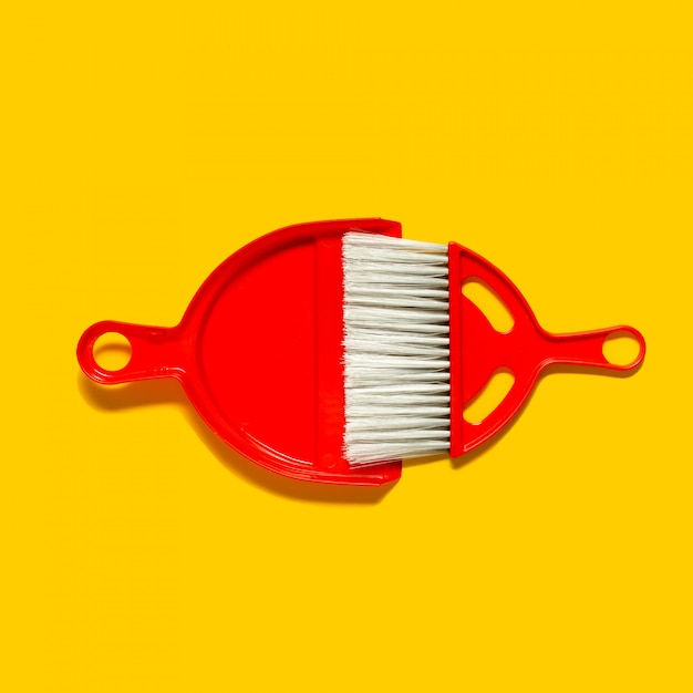 Red dustpan and brush lying on yellow surface. in the style of pop art