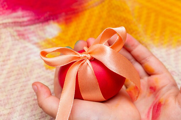 Red egg with bow in kids hands for the Easter