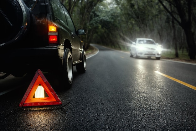 Red emergency stop sign red triangle warning sign and broken black SUV car on country road in summer rain