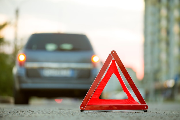 Red emergency triangle stop sign and broken car on a city street.