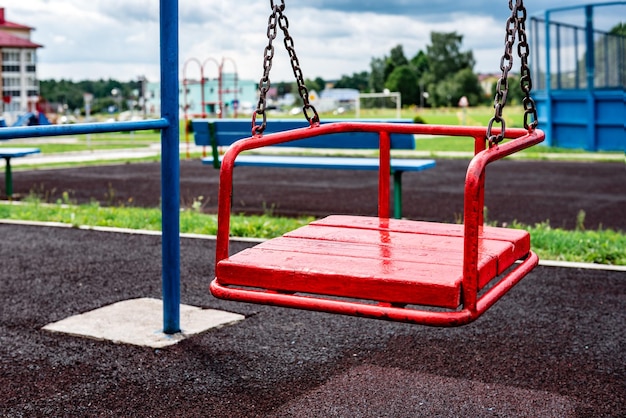 Red empty playground swing near school.