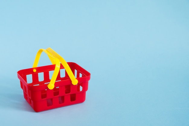 Red empty toy plastic shopping basket isolated on blue background. Sale and shopping concept. Copy space