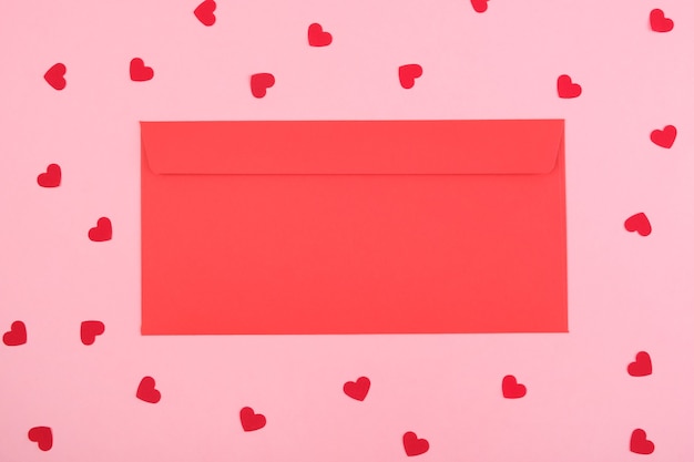 Red envelope on a pink background with hearts.Top view. Copy space. Festive Valentine's Day concept.